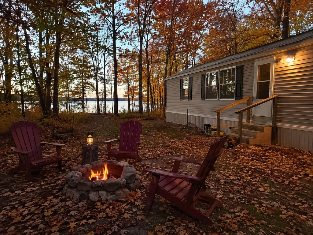 A cozy fire pit surrounded by chairs and a house with trees in the background.