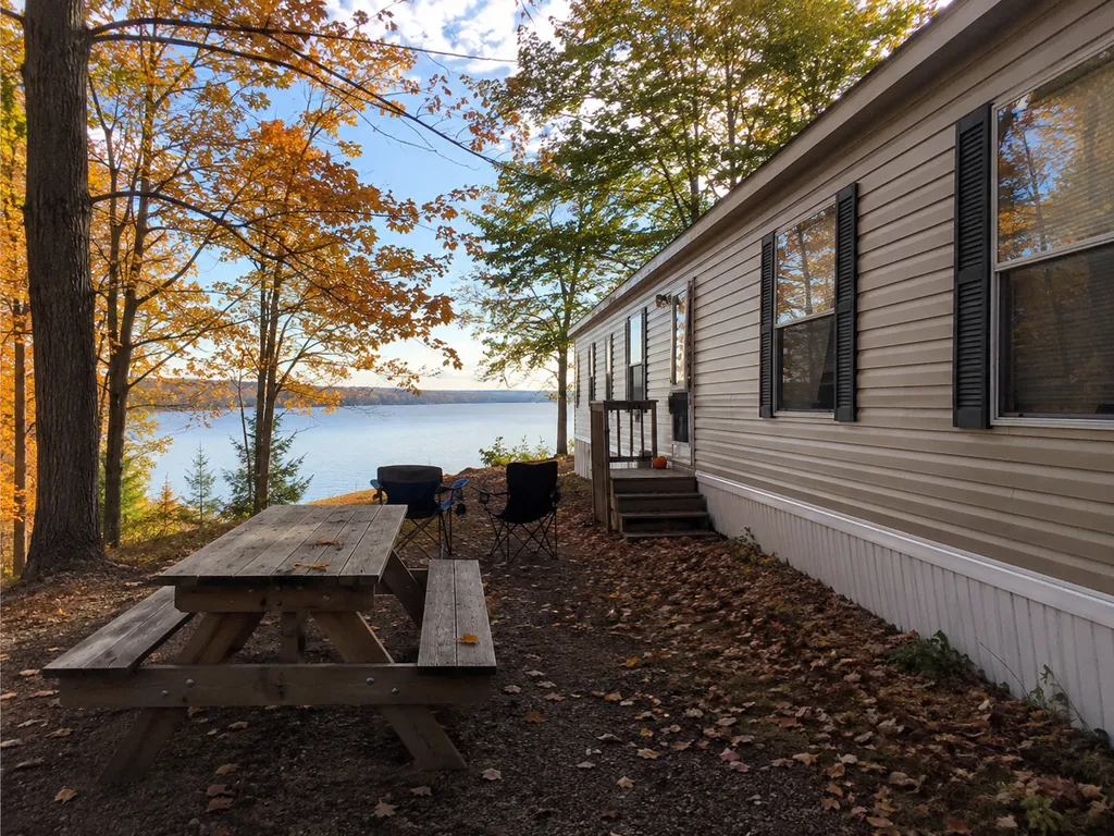 A lakeside trailer with a picnic table and chairs, surrounded by trees and a lake.