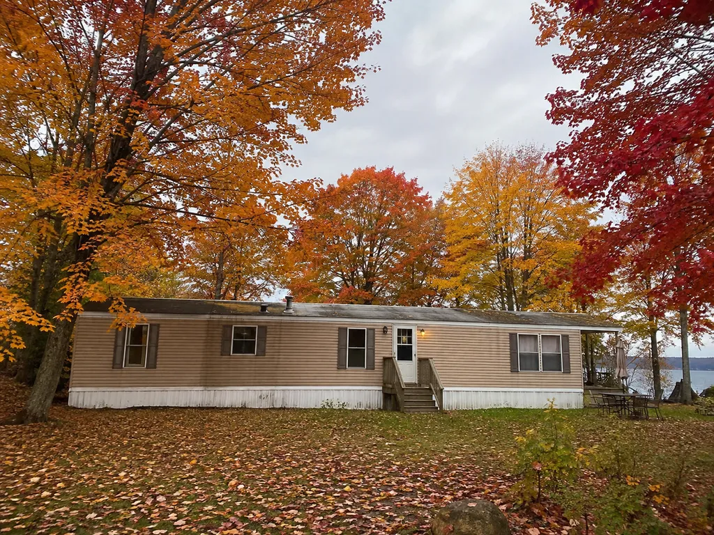 A small house surrounded by autumn trees with a lake in the background.